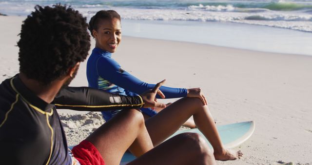 Couple having a relaxed and friendly conversation on beach during summer vacation. Both are seated on surfboards near shoreline. Useful for themes of leisure, travel, lifestyle, friendship, and surfing. Perfect for advertising travel destinations or illustrating outdoor activities in magazines.