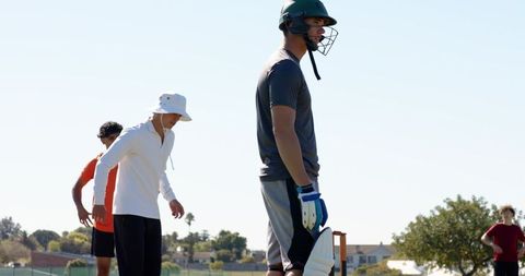 Young cricketer wearing helmet and pads preparing to bat on sunny outdoor practice field