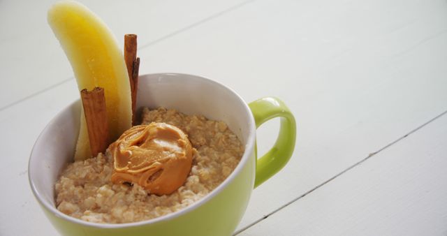 Healthy breakfast oatmeal topped with creamy peanut butter, banana slices, and cinnamon sticks in green cup. Ideal for articles about nutritious meals, healthy eating blogs, breakfast menus, and dietary advice content.