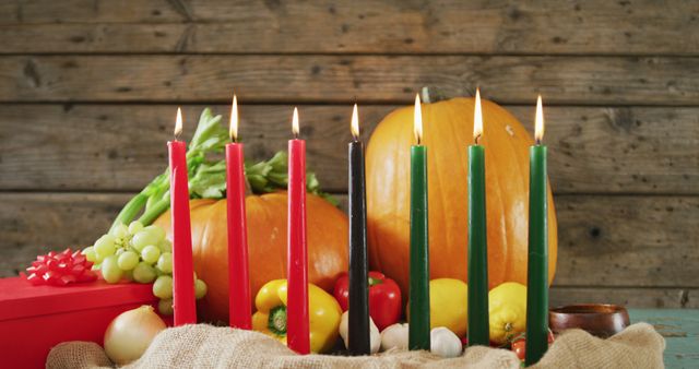 Colorful Kwanzaa candles arranged among fresh fruits and vegetables against a rustic wooden background. Perfect for illustrating cultural celebrations, holiday traditions, and diversity awareness. Suitable for use in educational materials, festive advertisements, and inclusive holiday greetings.