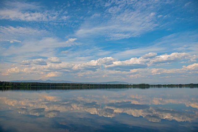 Beautiful cumulus clouds are reflecting on a tranquil lake. The stillness of the water mirrors the blue sky and creates a serene and peaceful scene. This setting is ideal for use in outdoor, travel, or landscape photography materials, conveying a sense of calm and natural beauty. It is also practical for motivational posters, nature magazines, or relaxation-themed projects.