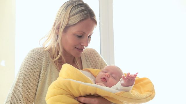 This engaging scene of a mother smiling happily as she lovingly holds her newborn baby wrapped in a cozy yellow blanket can be used in parenting blogs, websites about motherhood, and healthcare advertisements. It depicts maternal love, bonding, and family care, making it ideal for use in brochures and guides related to childbirth and parenting.