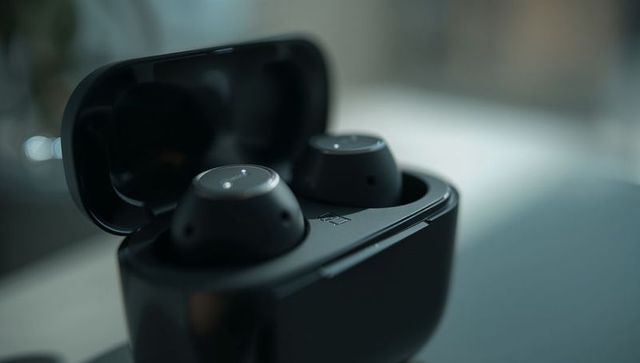 Matte black wireless earbuds in open charging case on tabletop closeup, bluetooth tech
