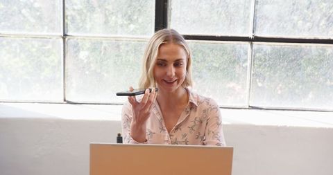 Businesswoman using smartphone voice assistant at office desk
