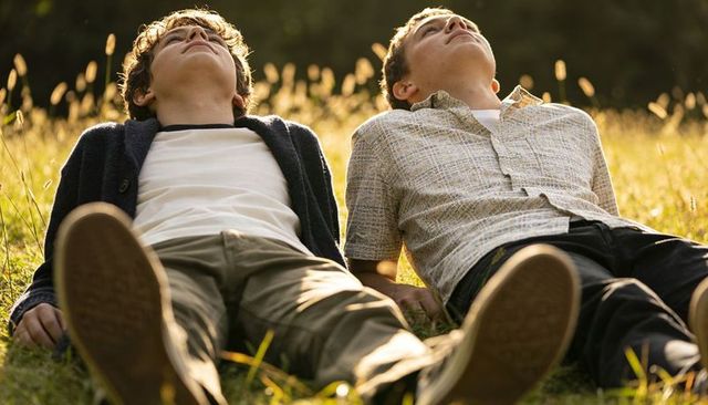 Teen friends reclining in sunlit meadow gazing skyward, casual clothing, relaxed mood
