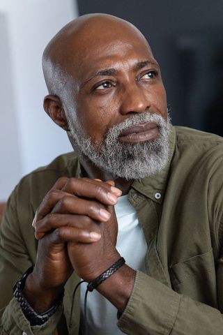 Reflective senior african man clasping hands, gazing thoughtfully, gray beard portrait