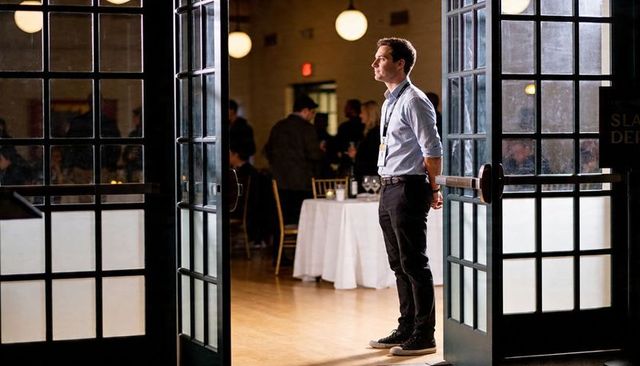 Standing event staffer monitoring banquet hall entrance through glass doors at reception