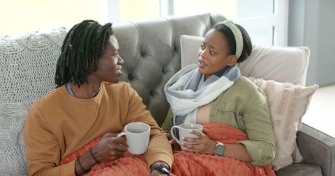 African american couple sharing warm drinks and conversation on cozy tufted sofa at home