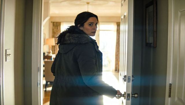 Woman leaving home wearing winter parka looking back at sunlit front door