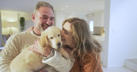 Smiling couple cuddling golden retriever puppy in modern living room