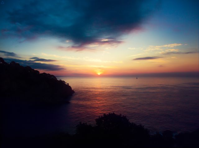 Sunset over calm sea with dramatic sky creating a serene atmosphere. Ideal for use in travel brochures, nature-themed websites, relaxation apps, or as a desktop background to evoke a sense of peace and tranquility.