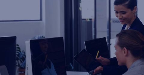 Female mentor guiding coworker with tablet and yellow stylus in modern office teamwork