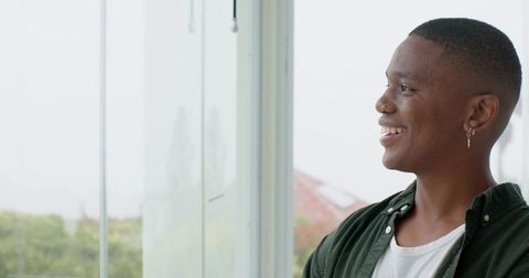 Smiling african american man looking out window in daylit home interior, casual green shirt