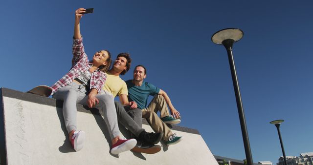 Group of friends sitting together at skate park taking selfie on bright sunny day. Perfect for illustrating themes of friendship, youth, outdoor activities, and enjoyable moments. Can be used for social media campaigns, advertisements, blog posts about leisure activities, or community events.