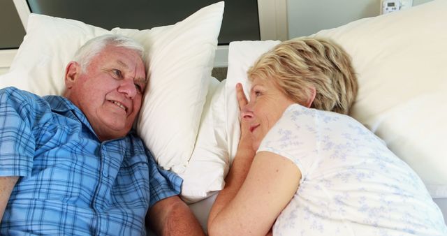 Elderly couple enjoying a relaxed moment in bed, sharing smiles and affection. Perfect for depicting senior life, love, healthy aging, and companionship in advertising, blogs, and caregiving services promotions.