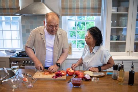 Asian couple preparing tomato and cheese on kitchen island during relaxed home cooking