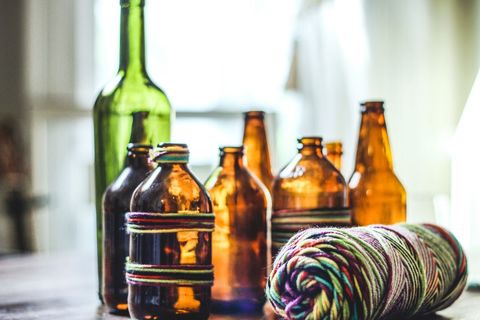 Recycled glass bottles with colorful threads on table