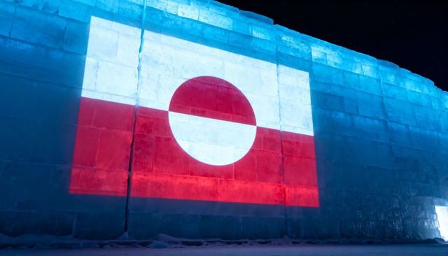 Greenland flag projected onto massive ice wall at night with blue lighting and snow