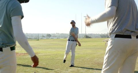 Baseball team warming up with pitcher throwing to teammates on sunlit grass practice field