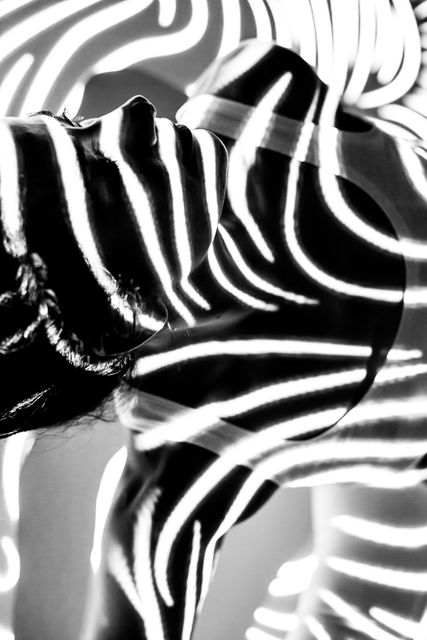Woman immersed in abstract black and white stripes resembling zebra patterns, creating a striking play of light and shadow. Perfect for modern art projects, interior design inspirations, creative advertising, or experimental photography collections.