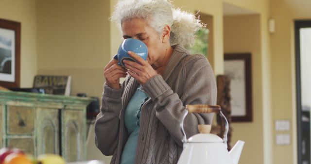 Portrait of senior biracial woman holding mug and drinking in kitchen. retirement and senior lifestyle, spending time alone at home.