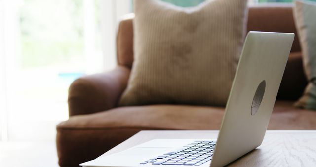 Open laptop on wooden coffee table in cozy living room. Perfect for themes related to remote work, home office setup, comfortable workspace, and modern technology. This can be used in blog articles about home productivity, technology reviews, or interior design tips focusing on comfortable and practical workspaces.