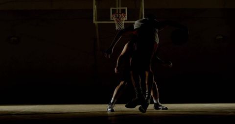 Silhouetted basketball players battling under hoop spotlight, dramatic court action