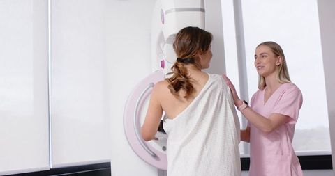 Radiology technician positioning patient for mammogram screening in clinical mammography suite