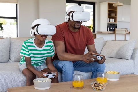 African american father and son playing virtual reality games on sofa with controllers