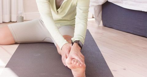 Woman stretching on yoga mat at home wearing smartwatch