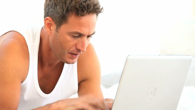 Man intensely typing and concentrating on work with laptop against a bright white background. Perfect for illustrating themes related to remote work, concentrated working environments, adult lifestyles, or home office settings.