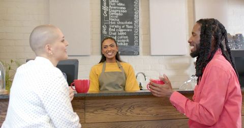 Smiling barista greeting diverse customers at rustic coffee counter with red mugs