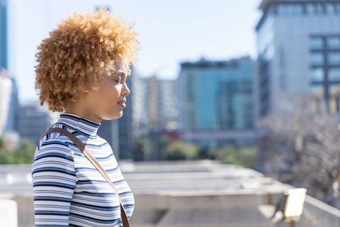 Sunlit african american woman on rooftop terrace wearing striped turtleneck, serene