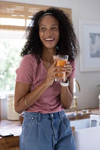 African american woman smiling holding glass of fresh orange juice in bright kitchen
