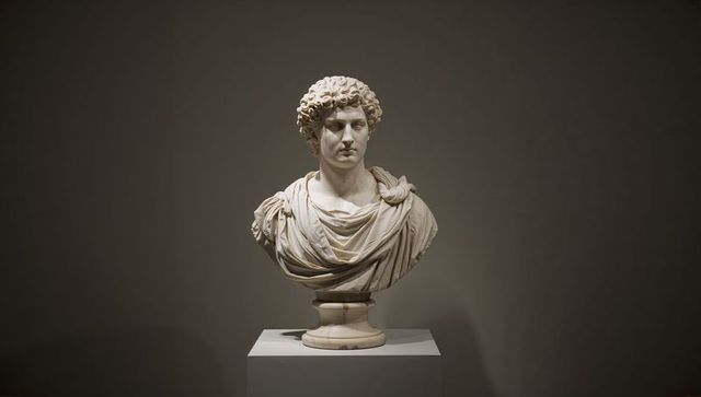 Classical marble bust of a figure with curly hair in museum gallery