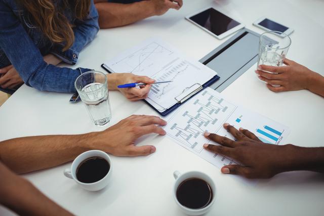 Business executives collaborating around a table, analyzing graphs and charts. Ideal for illustrating teamwork, business strategy, data analysis, and professional meetings. Useful for corporate presentations, business articles, and office-related content.