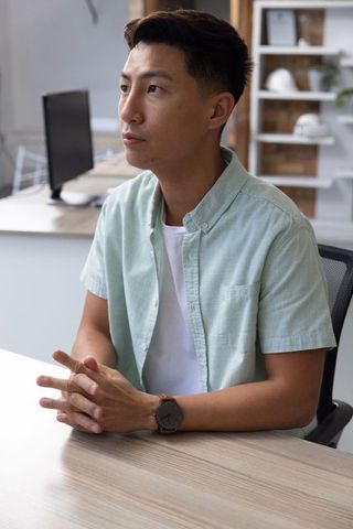 Asian Man in Green Shirt at Office Desk with Focused Expression