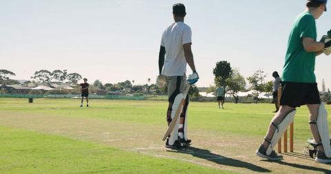 Cricket batsman running between wickets on sunny suburban park ground with fielders