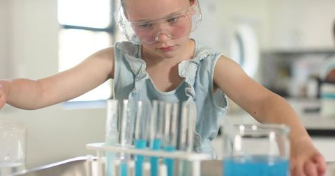 Young girl wearing safety goggles conducting colorful chemistry experiment with test tubes