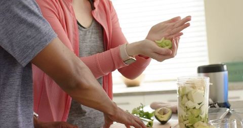 African american couple preparing avocado smoothie and guacamole in bright kitchen