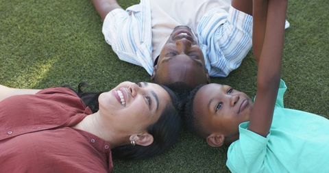 Lying on grass smiling mixed family sharing playful learning moment with child