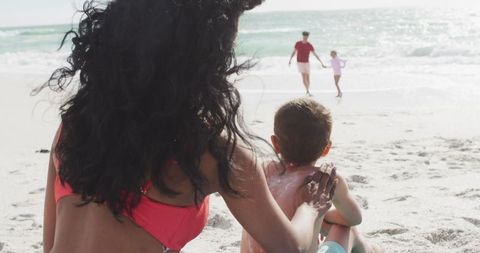 Hispanic Mother Applying Sunscreen to Son on Sunny Beach