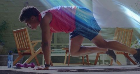 Man performing mountain climber exercise on backyard patio with dumbbells and water bottle