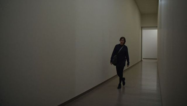 Solitary woman walking down minimalist gallery corridor toward open doorway