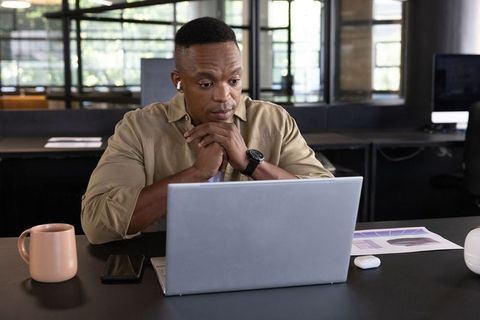 African american professional working on laptop in modern open-plan office with charts