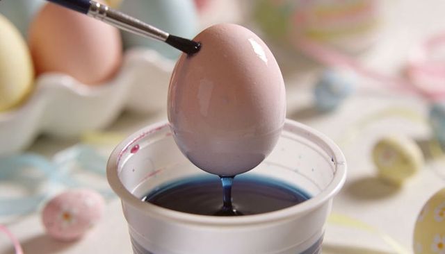 Painting Pastel Easter Egg with Brush and Blue Dye Close-Up on Craft Table