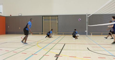 Multiracial men playing competitive indoor volleyball on school gym court with knee pads