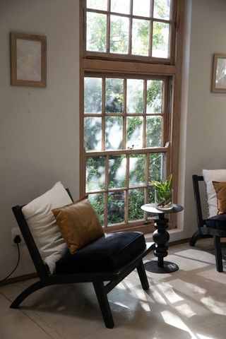 Sunlight streaming on cozy minimal lounge chair by sash window with tan pillow and plant