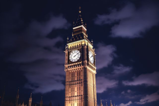 Big Ben clock tower illuminated against a night sky with clouds. Ideal for travel guides, promotional materials, British tourism campaigns, and educational resources about historic landmarks in London.
