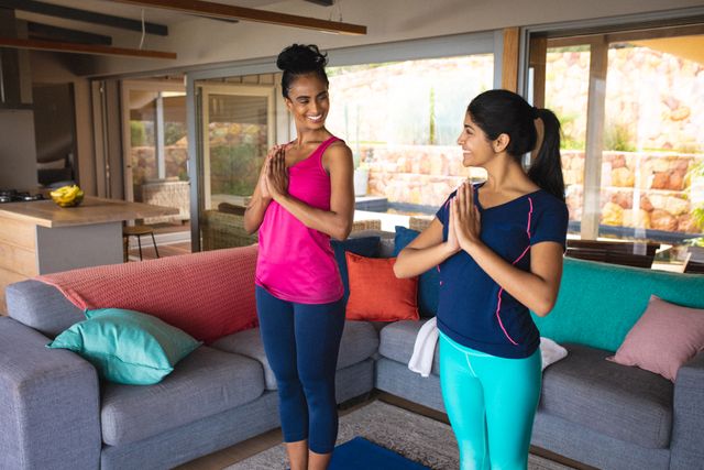 Biracial smiling mother and daughter looking at each other while meditating in living room. Unaltered, family, love, togetherness, thirsty, exercise, fitness, active lifestyle and home concept.